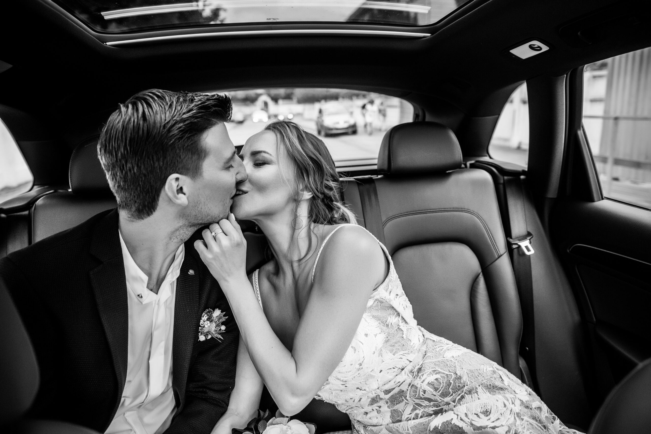 Hochzeitspaar nach der Trauung küsst sich im Auto am Weg zur Feier